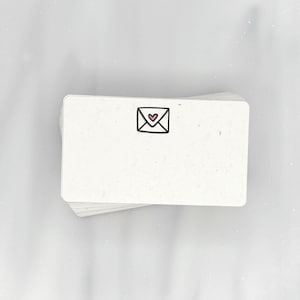 May include: A stack of white note cards with a small black and pink envelope with a heart inside printed on the front.