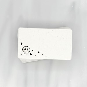 May include: A stack of blank white note cards with a black skull and stars design printed on the front.