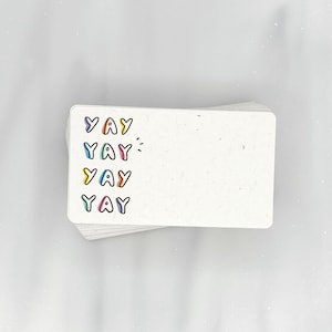 May include: A stack of white note cards with the word "YAY" written in colorful letters on the front.