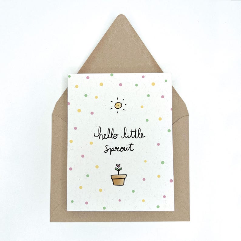 Peut inclure: Une carte blanche avec un motif de pois verts, jaunes et roses. La carte a un soleil avec un visage souriant, une plante en pot avec un c&oelig;ur et le texte "hello little sprout".