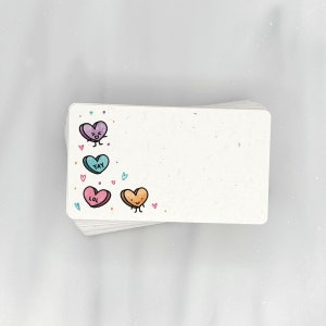 May include: A stack of white rectangular cards with rounded corners. Each card has a hand-drawn heart illustration in the corner. The hearts are purple, teal, pink, and orange, with the words "Yay" and "LOL" on them.