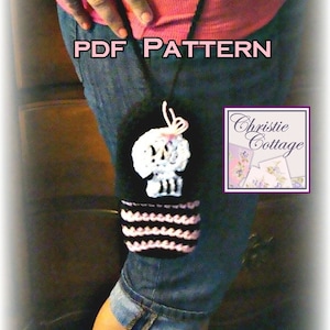 May include: A black and pink crocheted skull bottle cozy with a pink bow. The cozy is hanging from a black strap. The text "PDF PATTERN" is written in pink letters on a blue background. The text "Christie Cottage" is written in white letters on a purple background.