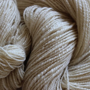 May include: A close-up of a skein of natural white yarn. The yarn is soft and fluffy, and it has a slightly textured surface.