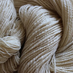 May include: A close-up of a skein of natural white yarn. The yarn is soft and fluffy, and it has a slightly textured surface.