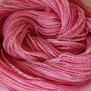 May include: A skein of pink and white yarn with a variegated color pattern. The yarn is soft and fluffy, and it is perfect for knitting or crocheting.