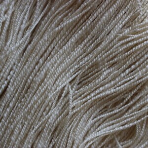 May include: Close-up of a bundle of cream-colored yarn. The yarn is soft and fluffy, and it is perfect for knitting or crocheting.
