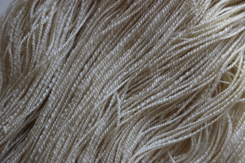 May include: Close-up of a bundle of cream-colored yarn. The yarn is soft and fluffy, and it is perfect for knitting or crocheting.