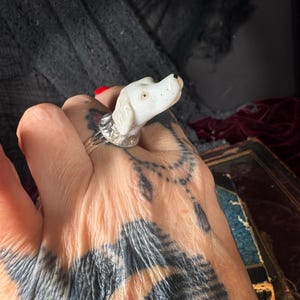 Peut inclure: Bague t&ecirc;te de chien en c&eacute;ramique blanche avec un anneau argent&eacute;. Le chien a des points noirs pour les narines et un point noir pour l'&oelig;il. Un bijou unique.