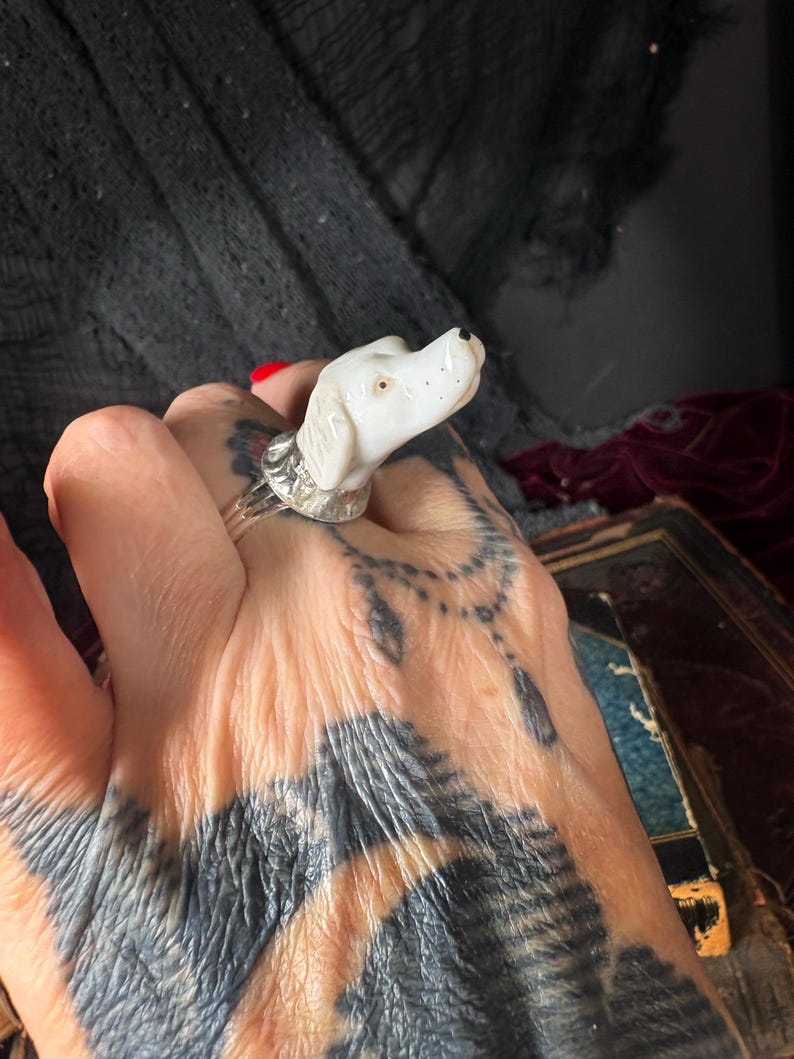 Peut inclure: Bague t&ecirc;te de chien en c&eacute;ramique blanche avec un anneau argent&eacute;. Le chien a des points noirs pour les narines et un point noir pour l'&oelig;il. Un bijou unique.