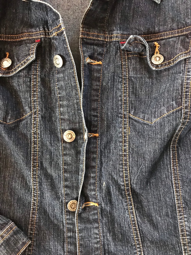 May include: A dark blue denim jacket with a button closure and two front pockets.