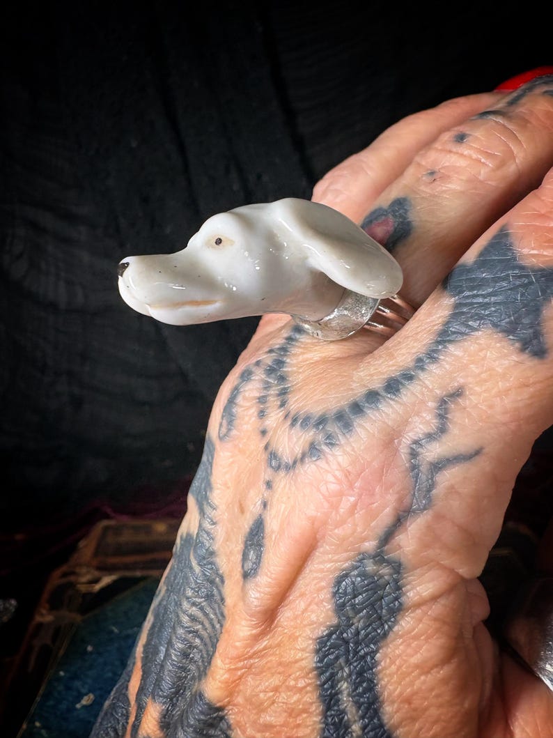 Peut inclure: Bague t&ecirc;te de chien en c&eacute;ramique blanche avec un anneau argent&eacute;. La t&ecirc;te de chien est d&eacute;taill&eacute;e avec un nez noir et un petit point marron pour l'&oelig;il. Un bijou unique.