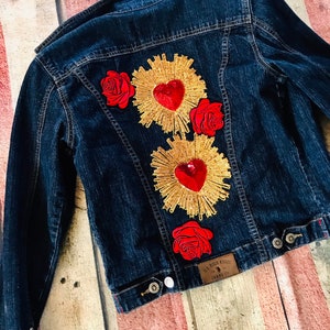 May include: A dark blue denim jacket with three red roses and two gold heart-shaped embellishments on the back. The jacket has a label that reads "US Polo Assn. Jeans Co."