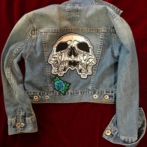 May include: A blue denim jacket with a white skull patch and a blue rose patch on the back.