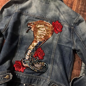May include: A blue denim jacket with a sequined cobra and red roses embroidered on the back.