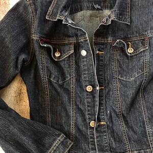 May include: A dark blue denim jacket with red stitching and silver buttons. The jacket has a U.S. Polo Assn. Jeans Co. label on the front.