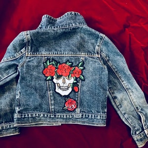 May include: A blue denim jacket with a skull and red roses embroidered on the back.