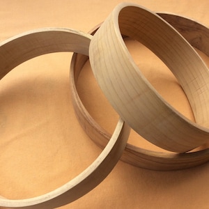 Könnte beinhalten: Drei Holzreifen in verschiedenen Größen, übereinander gestapelt. Die Reifen sind aus hellbraunem Holz und haben eine glatte, polierte Oberfläche.