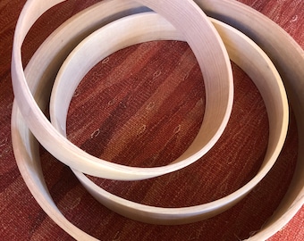 May include: Three wooden drum hoops of different sizes, nested together. The hoops are made of light-colored wood and have a smooth, polished finish.