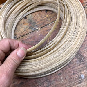 Peut inclure: Une longueur enroulée de matériau plat, flexible, translucide et beige clair avec une surface texturée. La bande est enroulée en forme circulaire, montrant plusieurs couches du même matériau empilées en une spirale continue et uniforme.