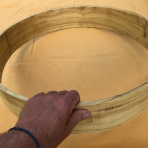 May include: A natural wood drum hoop, with a light brown colour and a smooth, polished finish. The hoop is curved and has a slight grain pattern.