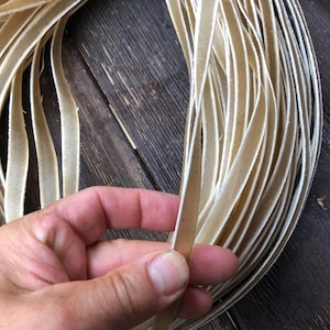 May include: A close-up of a bundle of off-white leather strips. The strips are about 1/2 inch wide and are arranged in a neat pile. The leather is soft and supple, and it has a natural, unpolished finish.