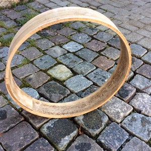 Peut inclure: Un cercle en bois pour un tambour, posé sur une surface pavée. Le cercle est en bois brun clair et a une finition naturelle. Il est légèrement patiné et montre des signes d'utilisation.