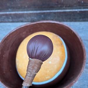 May include: A brown leather-covered mallet with a wooden handle, used for playing a large, round, brown clay drum.