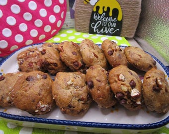 May include: A rectangular platter holds a collection of baked cookies. The cookies are oval-shaped, with a light brown color, and studded with chocolate chips and nuts. A sign that says "Welcome to our Hive" is in the background.