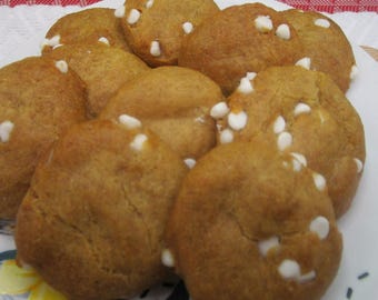 May include: A pile of round, golden-brown baked cookies featuring small, white chocolate chips embedded throughout the surface. The cookies have a textured, slightly uneven appearance and are arranged in a cluster on a white plate.