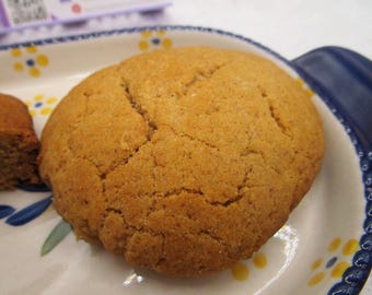 May include: A close-up of a round, golden brown cookie on a white plate with blue and yellow floral designs. The cookie has a slightly cracked surface.
