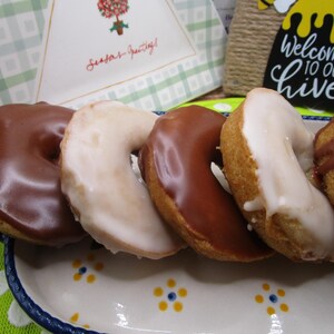 Puede incluir: Una fila de cinco galletas en forma de media luna dispuestas en una bandeja rectangular de cer&aacute;mica con un patr&oacute;n floral. Tres galletas est&aacute;n cubiertas con un glaseado de chocolate con leche, mientras que dos tienen un acabado de glaseado de az&uacute;car blanco.