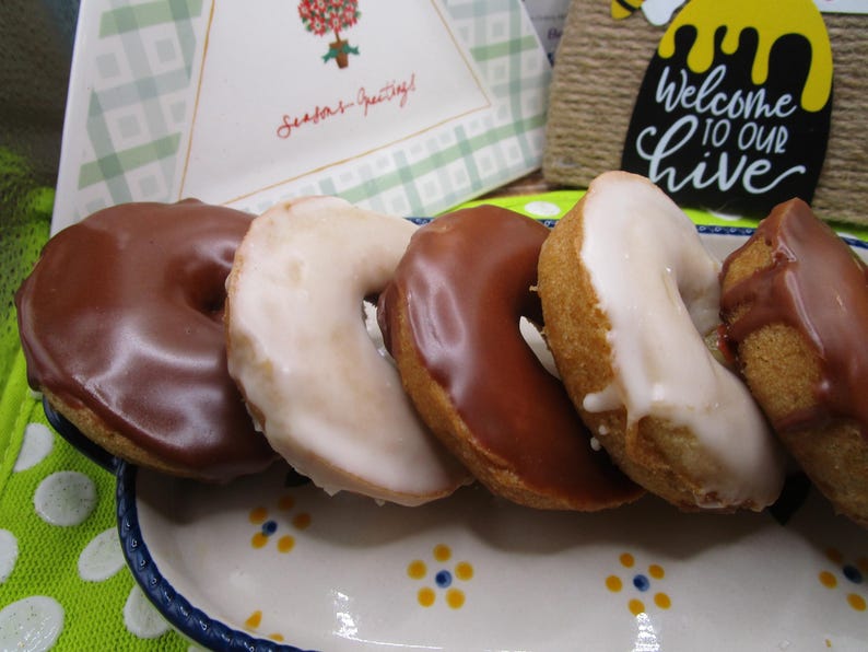 Puede incluir: Una fila de cinco galletas en forma de media luna dispuestas en una bandeja rectangular de cer&aacute;mica con un patr&oacute;n floral. Tres galletas est&aacute;n cubiertas con un glaseado de chocolate con leche, mientras que dos tienen un acabado de glaseado de az&uacute;car blanco.