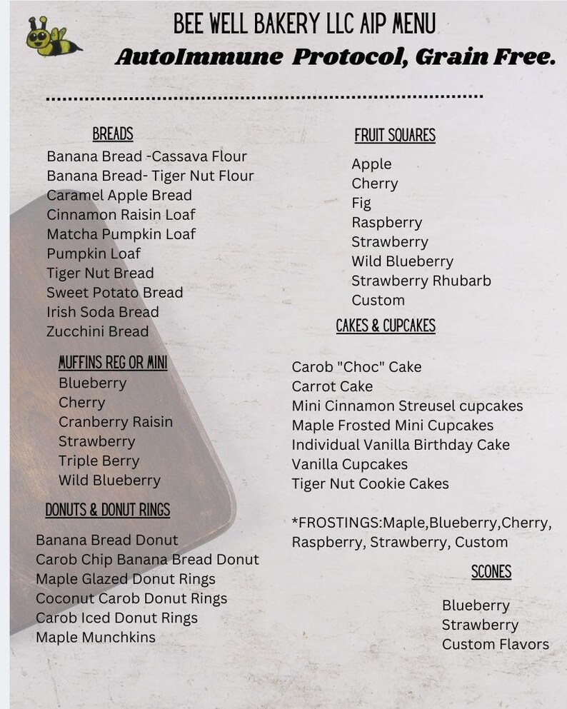 May include: A printed menu for Bee Well Bakery LLC featuring an AutoImmune Protocol and grain-free list of items including breads, muffins, donuts, fruit squares, cakes, cupcakes, and scones, with a small cartoon bee graphic at the top left corner.