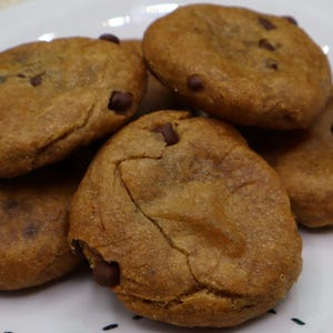 May include: A plate of freshly baked chocolate chip cookies. The cookies are golden brown with visible chocolate chips. They are arranged on a white plate with a decorative edge, suggesting a homemade treat.