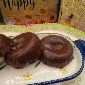 May include: Three chocolate glazed donuts on a white and blue floral patterned plate. The donuts are arranged in a row, with the largest donut in the back and the smallest donut in the front.