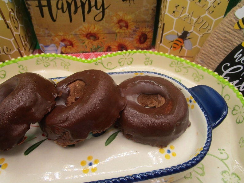 May include: Three chocolate glazed donuts on a white and blue floral patterned plate. The donuts are arranged in a row, with the largest donut in the back and the smallest donut in the front.