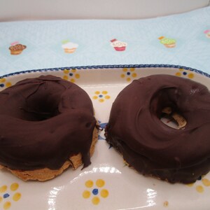 May include: Two chocolate-covered donuts on a white and blue patterned plate. The donuts are round with a hole in the center and are covered in a thick layer of dark chocolate.