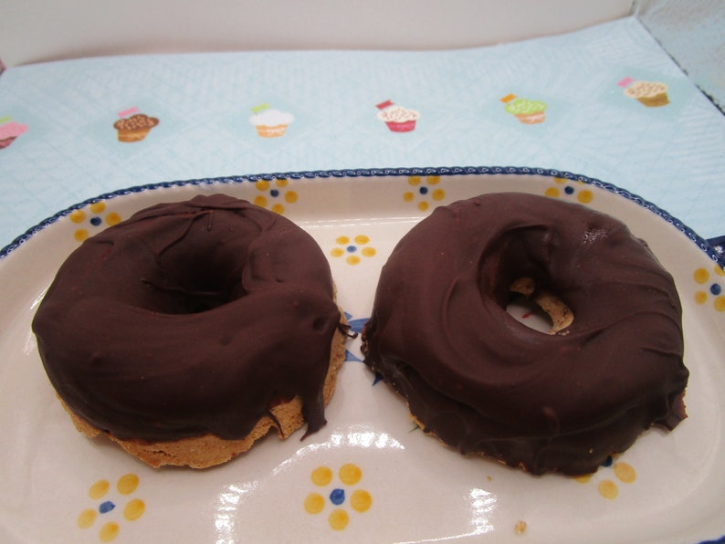 May include: Two chocolate-covered donuts on a white and blue patterned plate. The donuts are round with a hole in the center and are covered in a thick layer of dark chocolate.
