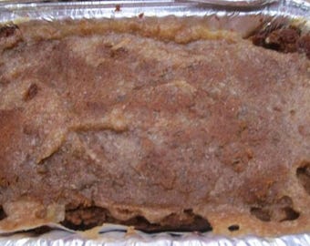 May include: A rectangular aluminum foil container filled with a baked brown food item. The top surface has a textured, light brown, slightly glossy crust that covers the darker, denser brown contents underneath within the metal pan.