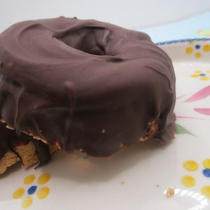 May include: Two chocolate-covered donuts on a white plate with a floral design. The donuts are stacked on top of each other and have a rich, dark chocolate glaze.
