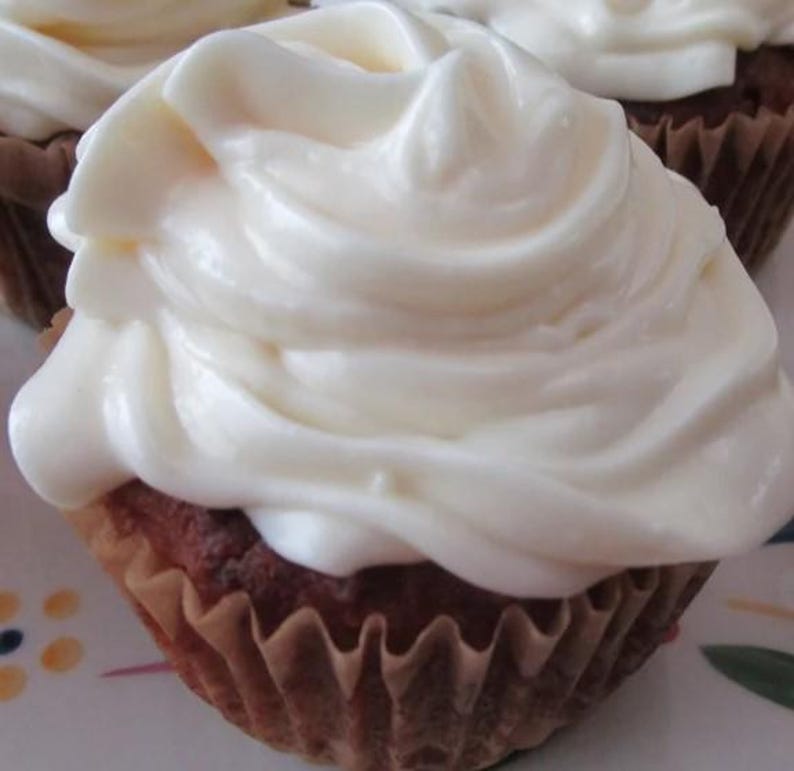 May include: A single cupcake featuring a golden-brown baked base held in a pleated brown paper liner, topped with a generous, thick swirl of smooth, opaque white frosting that covers the entire top surface of the cake in a decorative pattern.
