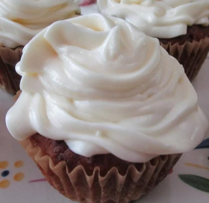 May include: A brown cupcake topped with a generous swirl of thick, white frosting. The cupcake is encased in a pleated, light brown paper liner. The frosting is applied in a smooth, continuous motion, creating soft ridges and peaks across the top.