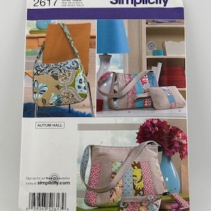 May include: Simplicity sewing pattern with images of bags in different styles. The bags have floral and patchwork designs in blue, green, and pink. The pattern includes a shoulder bag, tote, and small wallet.