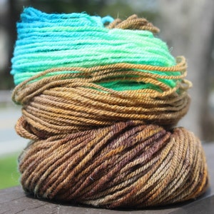May include: A skein of yarn with a gradient of teal, green, and brown colors. The yarn is wound into a ball shape.