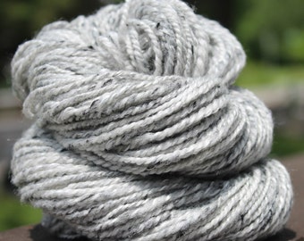 Puede incluir: Un ovillo de hilo blanco con motas negras. El hilo está retorcido y apilado en una bola suelta.