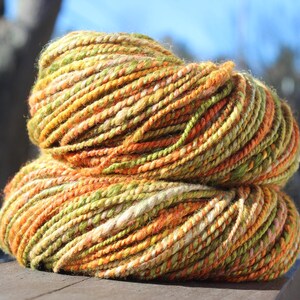 May include: A skein of yarn in shades of orange, green, and cream. The yarn is hand-spun and has a rustic, natural look.