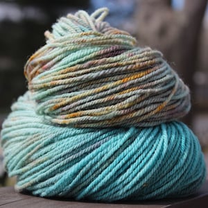 Peut inclure: Deux écheveaux de fil, un bleu sarcelle et un autre avec un motif chiné de sarcelle, vert, marron et orange.