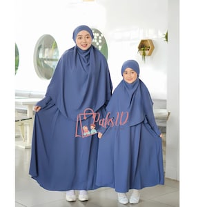 Op de afbeelding: Twee mensen dragen bijpassende blauwe abaya's met lange mouwen en bijpassende blauwe hoofddoeken. De abaya's zijn lang en hebben een eenvoudig ontwerp. De hoofddoeken zijn met een losse knoop om de nek gebonden.