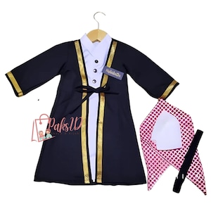 May include: A black and white outfit for a child, featuring a long-sleeved robe with gold trim, a white undershirt, a white cap, and a pink and white patterned scarf. The robe has a label that says "HabibiDic".