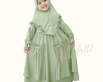 May include: A young girl wearing a light green dress with ruffles and a matching light green hijab. The dress has a layered skirt and long sleeves.